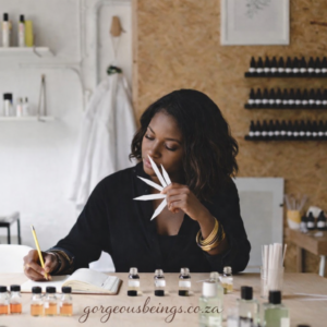 Black perfumer smelling fragrance blotters while taking notes during scent evaluation in a studio.
