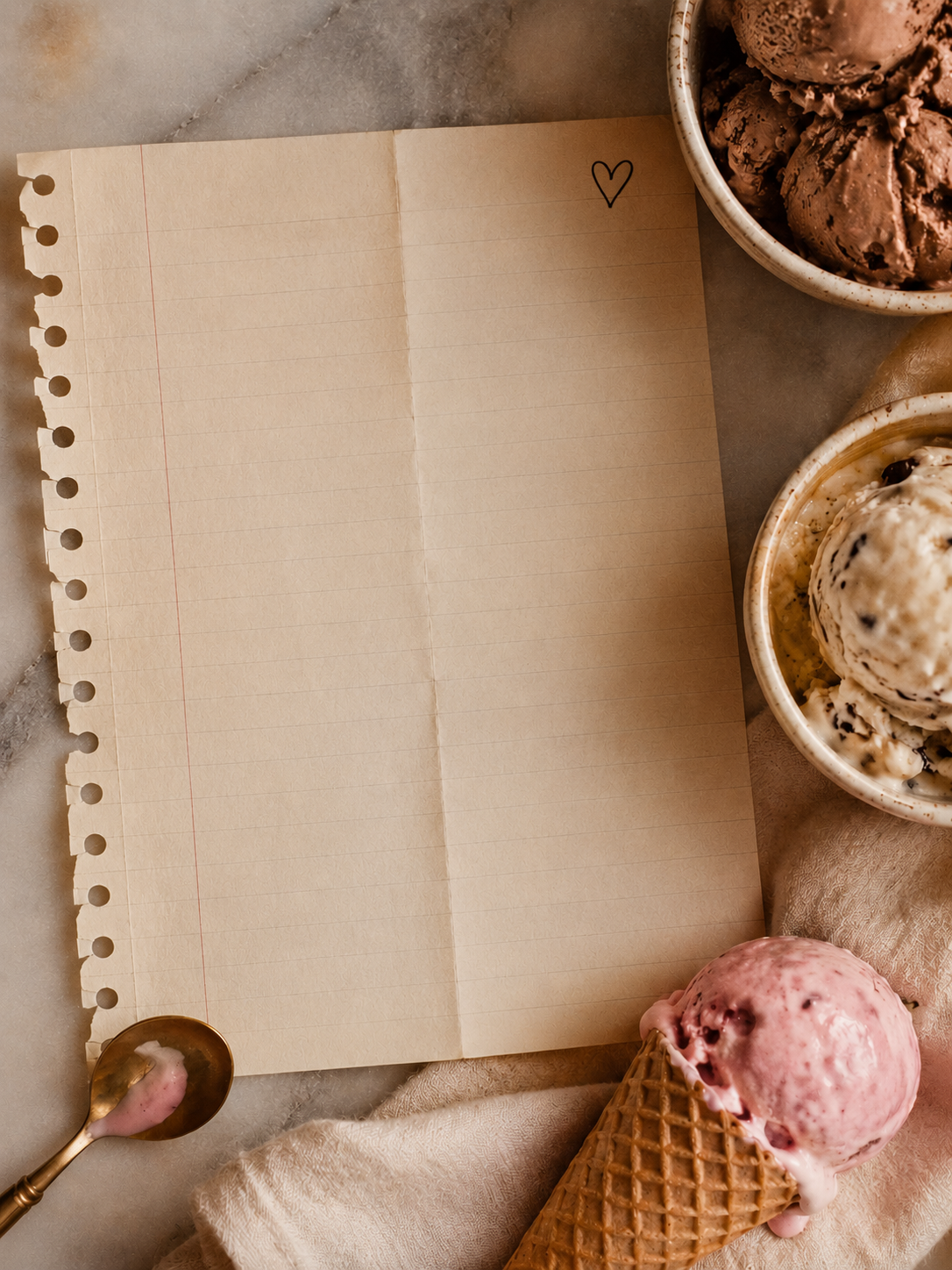 Blank lined notebook page surrounded by bowls of ice cream, a waffle cone, and a spoon on a warm-toned tabletop.